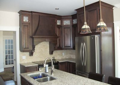 Armoires de cuisine en merisier teintes, portes avec centre plein, hotte style victorienne, ainsi qu’un comptoir en granite.