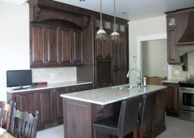 Armoires de cuisine en merisier teintes, portes avec centre plein, hotte style victorienne, ainsi qu’un comptoir en granite.